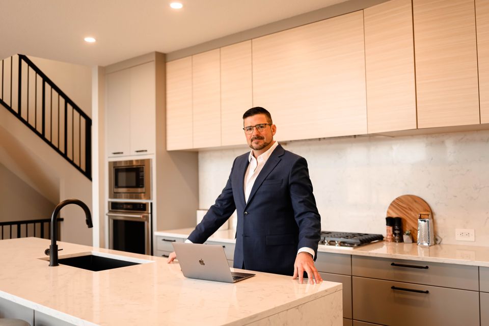 Ezra Malo, Calgary REALTOR® with RE/MAX First, standing at a kitchen island with his laptop