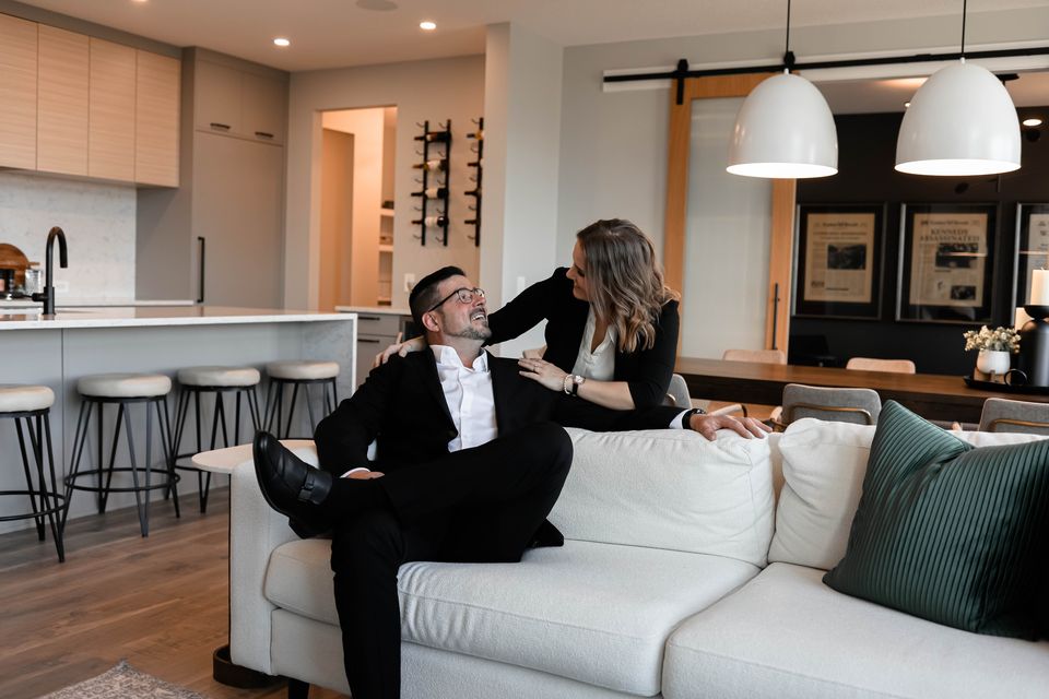 Ezra Malo and Whitney Mason, Calgary REALTORS® with the Ezra Malo Group at RE/MAX First, relaxing on a white sofa in a bright open-plan home